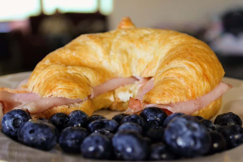 ham and cheese croissant sandwich on plate with blueberries