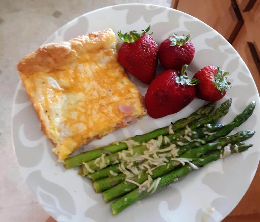 A square of egg dish, asparagus, and whole strawberries on a plate.