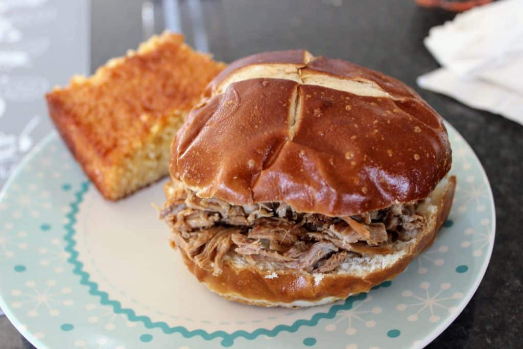 pulled pork on a pretzel bun and a slice of cornbread on a plate