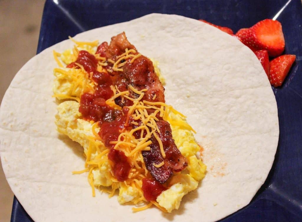 breakfast burrito on a blue plate with sliced strawberries