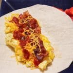 breakfast burrito on a blue plate with sliced strawberries