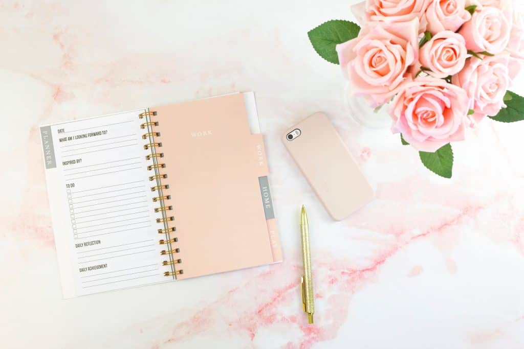 an open planner, pen, cell phone, and pink roses on marble counter