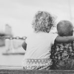 toddler sitting next to baby with arm around him