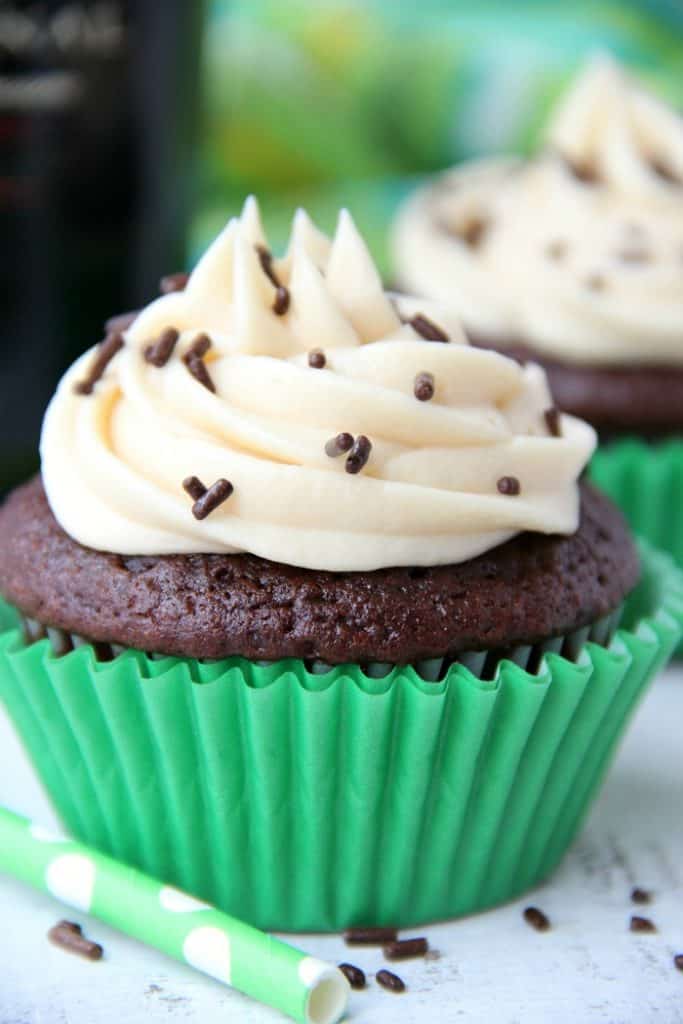 guinness cupcake in green wrapper with white frosting and chocolate sprinkles