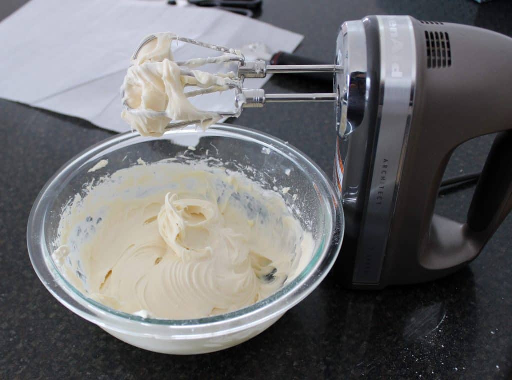 cream cheese frosting in mixing bowl next to electric hand mixer