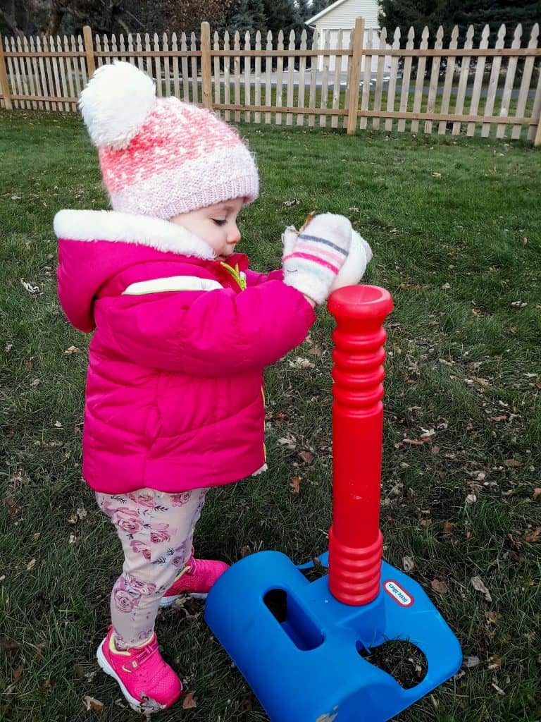 toddler in winter jacket playing t-ball