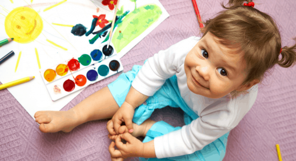 toddler sitting next to paints and a picture