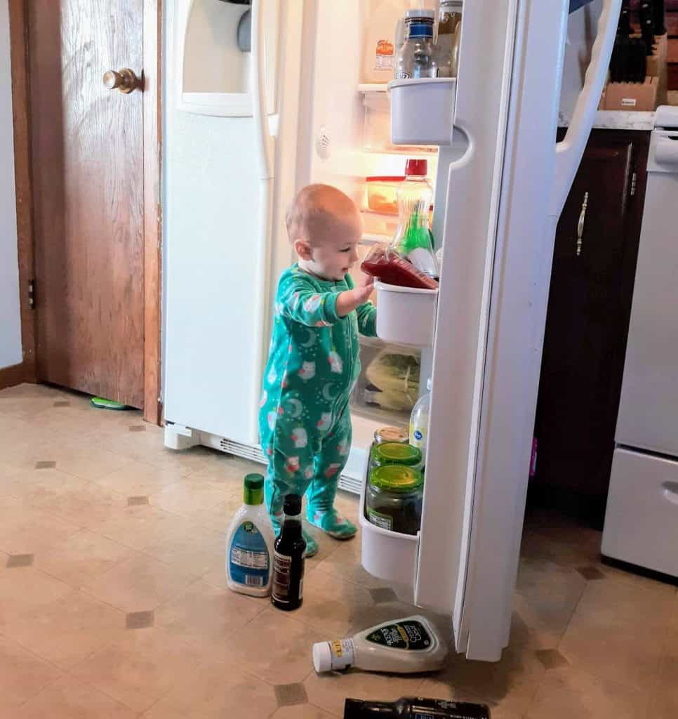 toddler in pajamas taking bottles out of the refrigerator