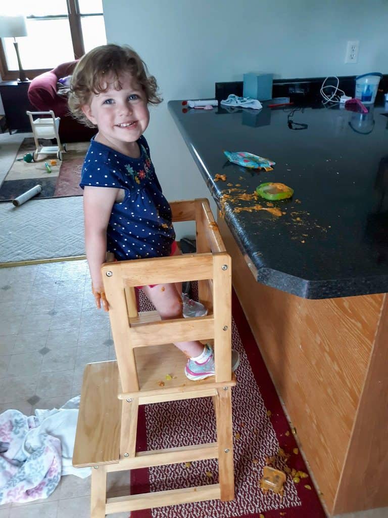 Toddler standing in a safety stool at kitchen counter.