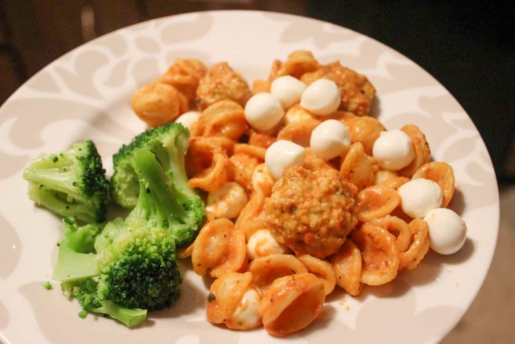 plate of noodles with meatballs and mozzarella pearls with a side of broccoli