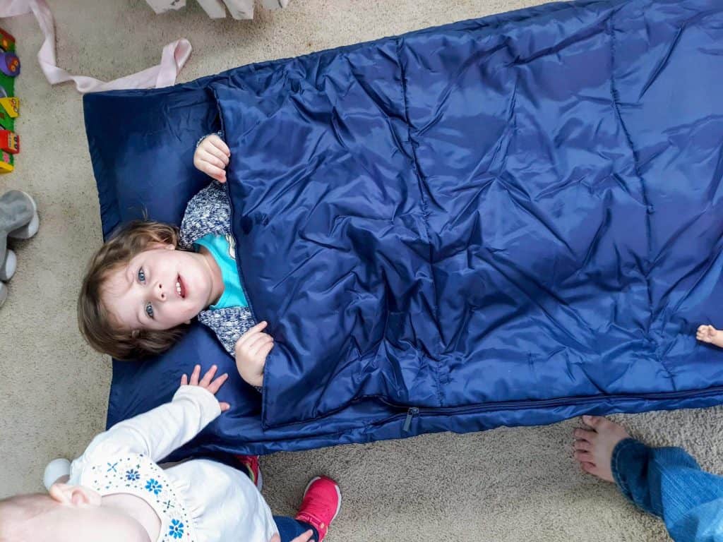 Toddler inside sleeping bag on cot.