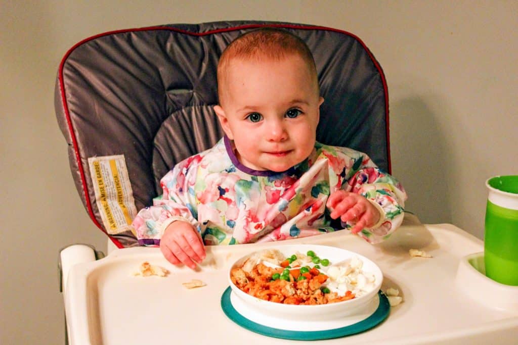 Toddler in long-sleeve bib in high chair.