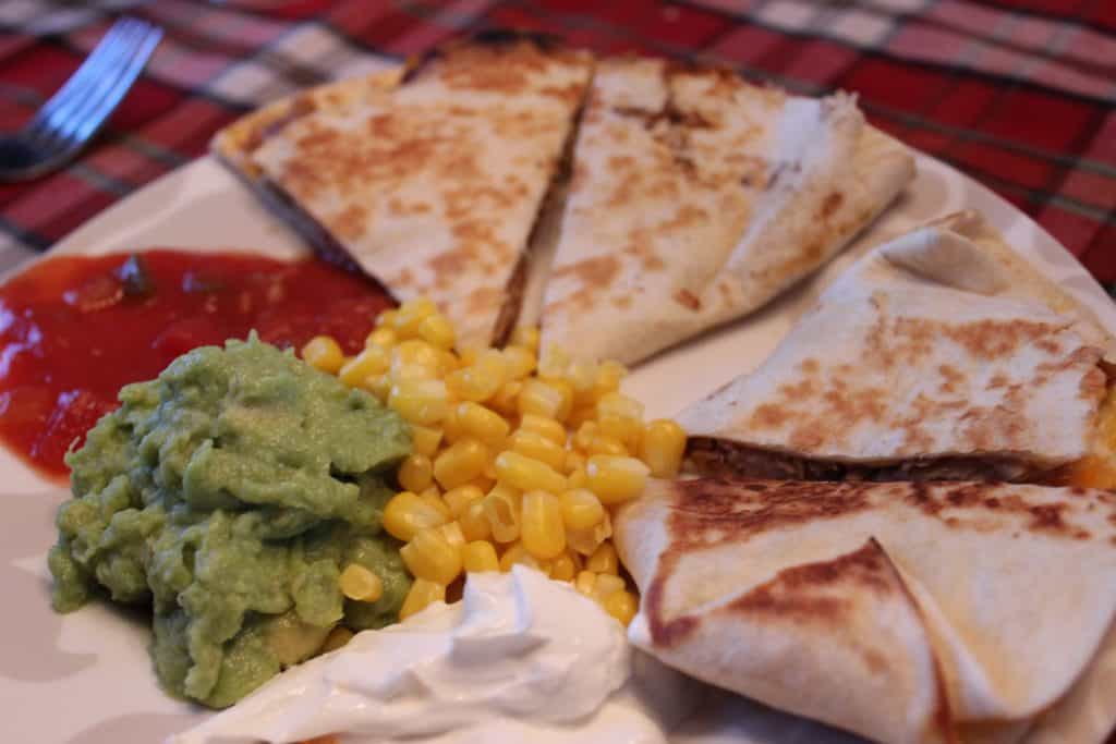 quesadilla on a plate with corn, guacamole, sour cream, and salsa