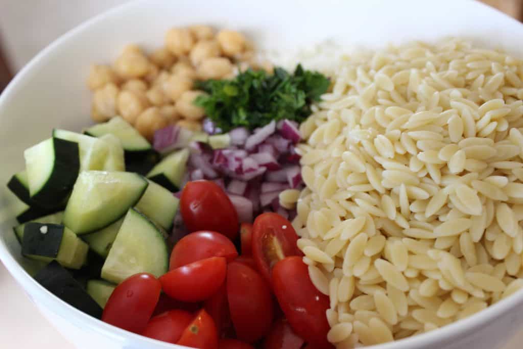 ingredients of orzo salad in a white bowl