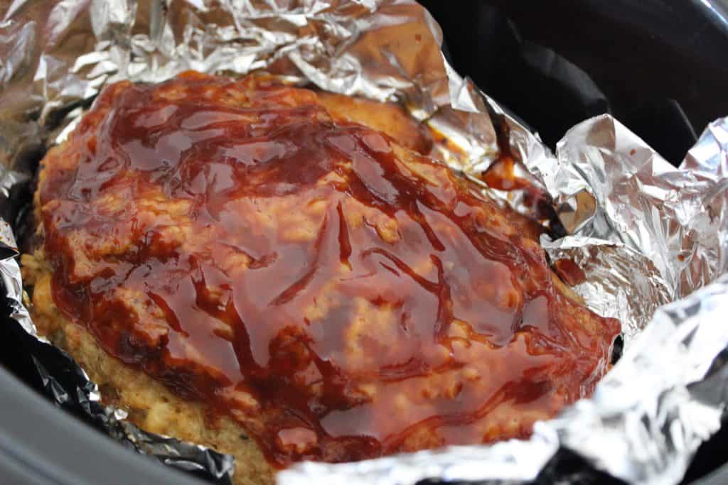 meatloaf covered in sauce cooking in a foil-line slow cooker