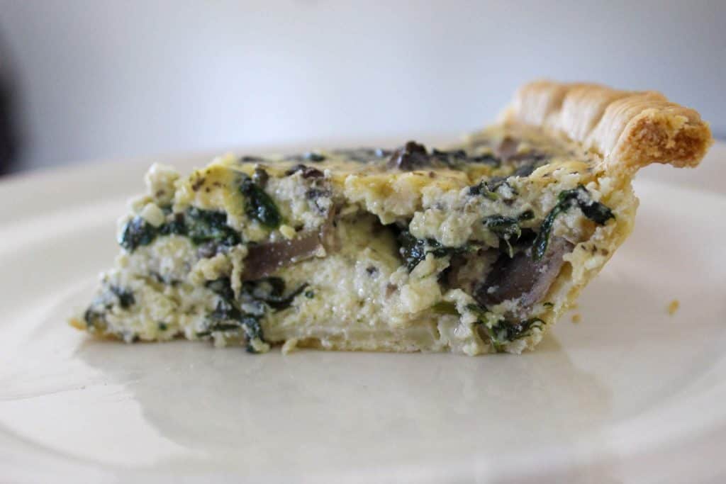 a slice of spinach mushroom quiche on a plate