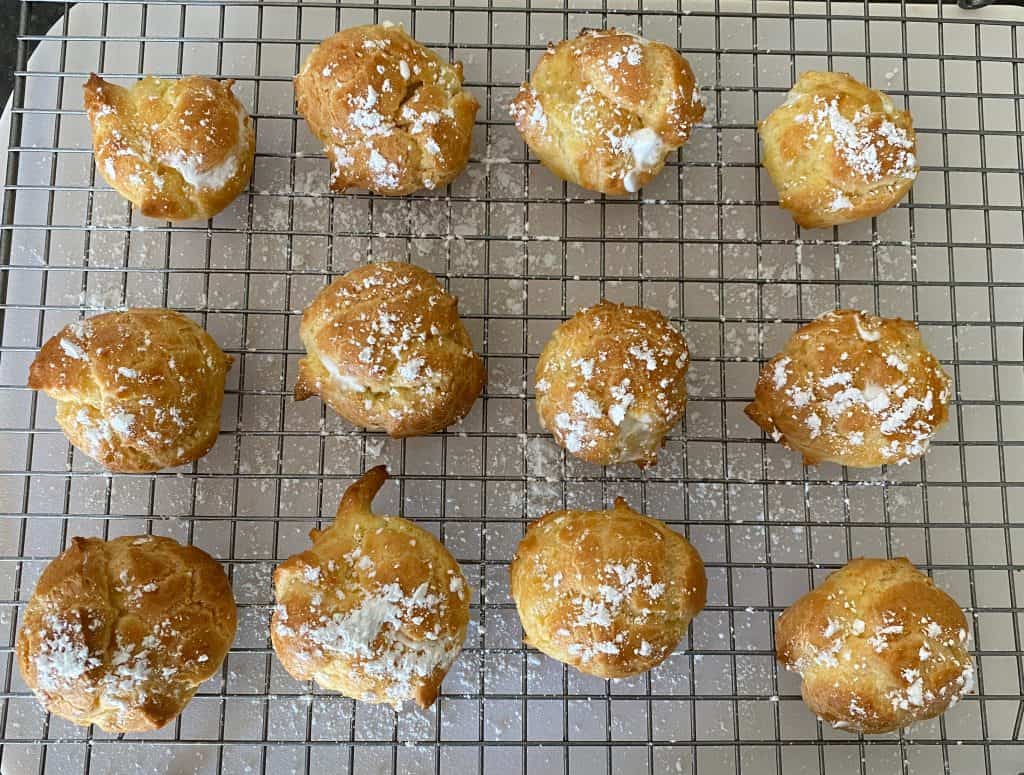 cream puffs sprinkled with powdered sugar on cooling rack