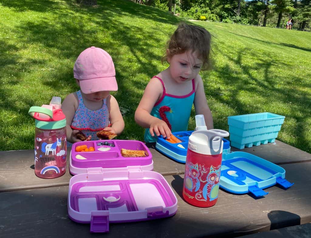 two toddlers eating lunch on a picnic table