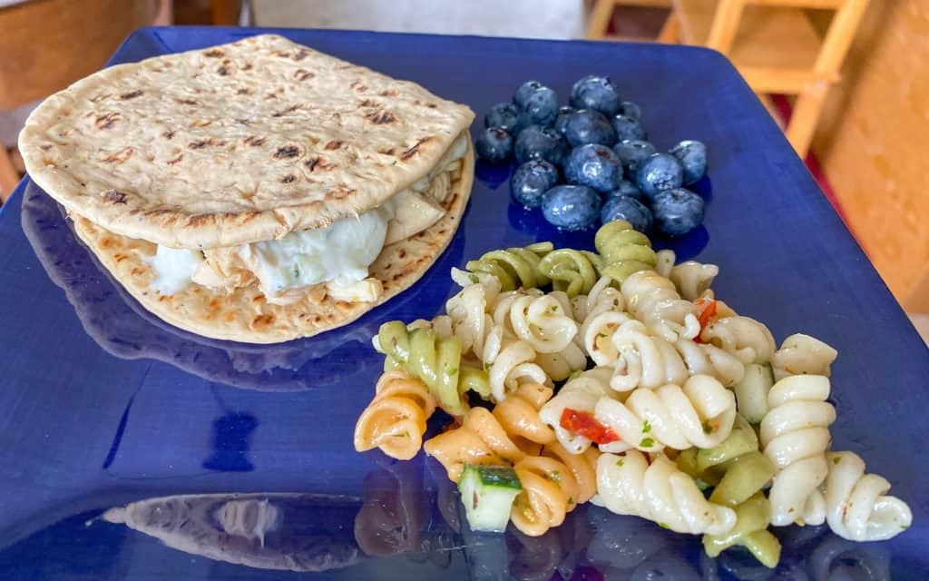 blue plate with a chicken gyro, blueberries, and pasta salad