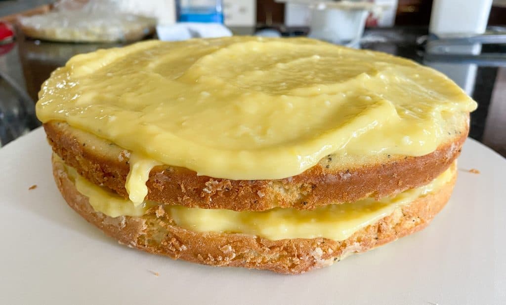 lemon curd spread on top of two layers of lemon poppy seed cake