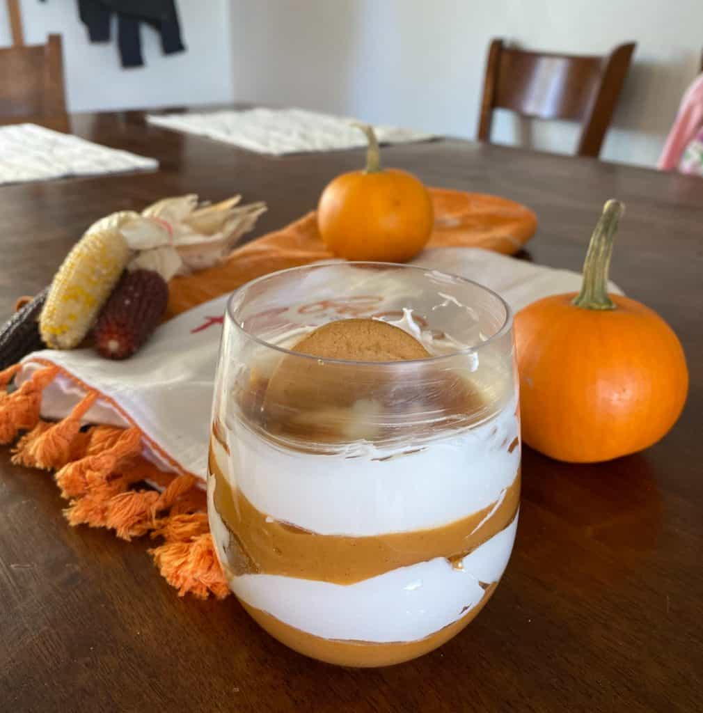 stemless glass with the pumpkin pudding parfait in it surrounded my mini corn and mini pumpkins