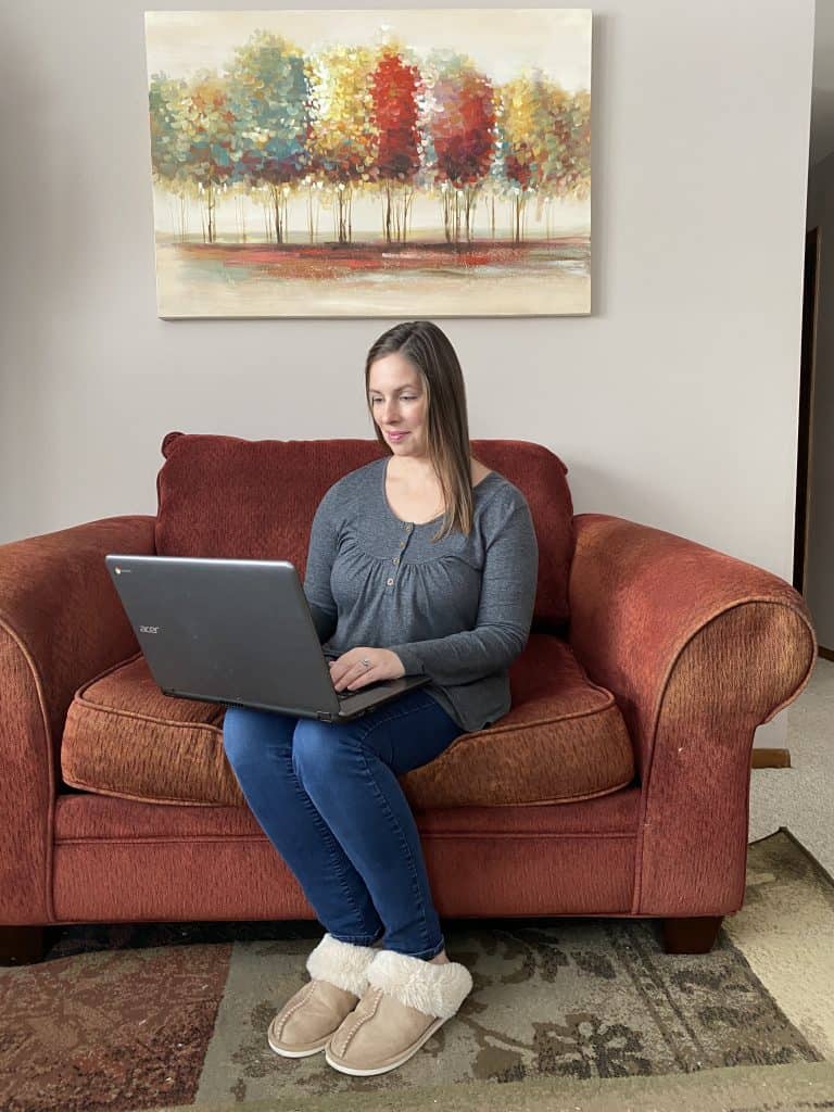 woman sitting on loveseat using laptop