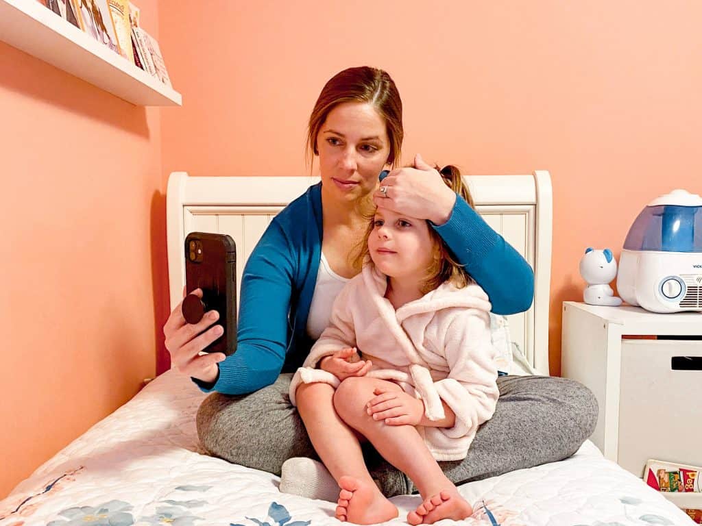 Mom sitting on a bed with child in her lap looking at cellphone