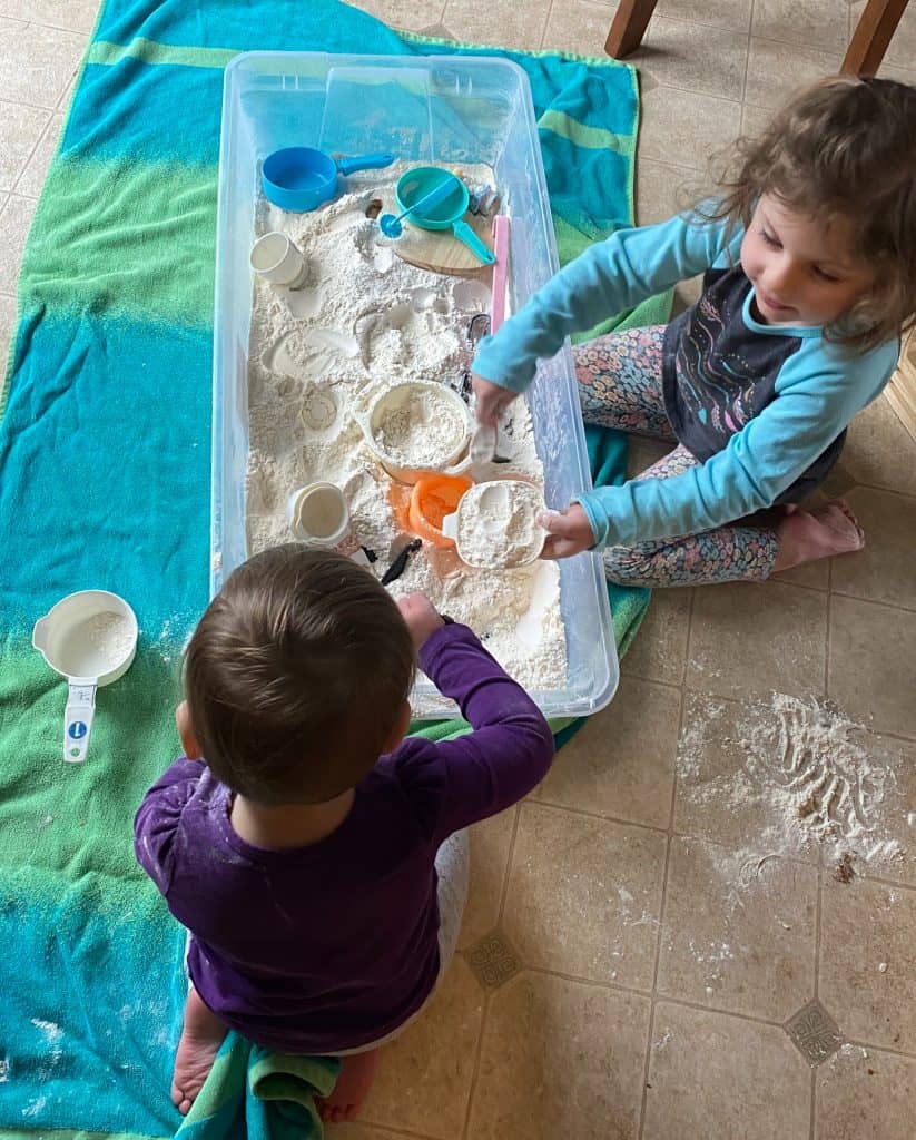 two kids playing in a flour sensory bin