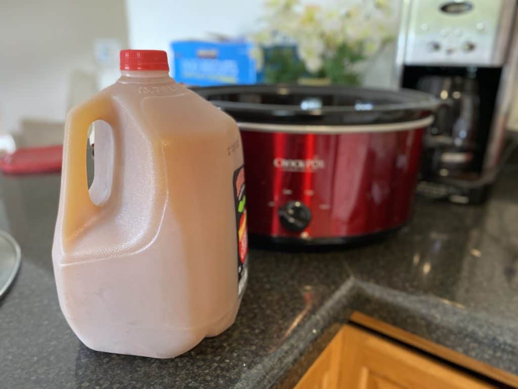 gallon of apple cider sitting on counter in front of slow cooker