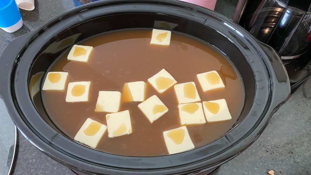 slow cooker full of apple cider and slices of butter