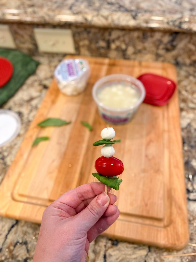 one mini caprese skewer with ingredients in the background