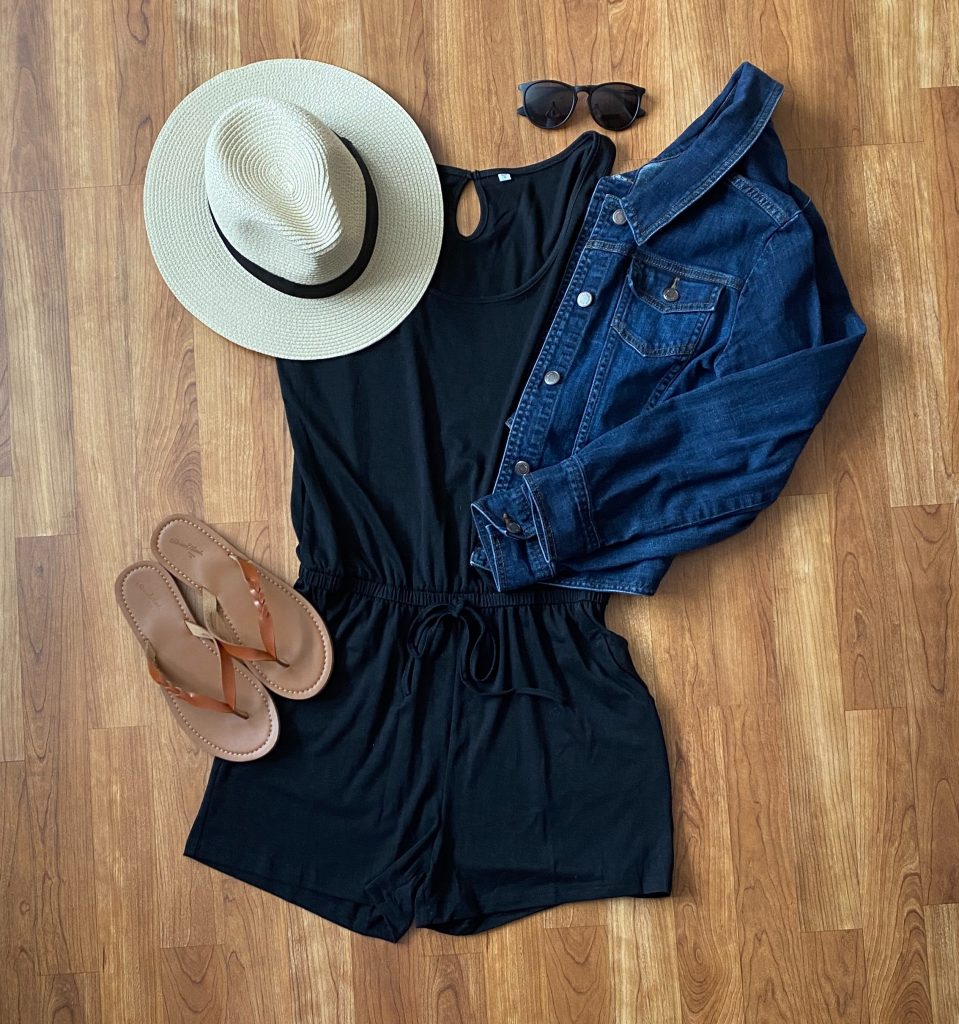 summer outfit consisting of a black romper, summer hat, jean jacket, sunglasses, and sandals
