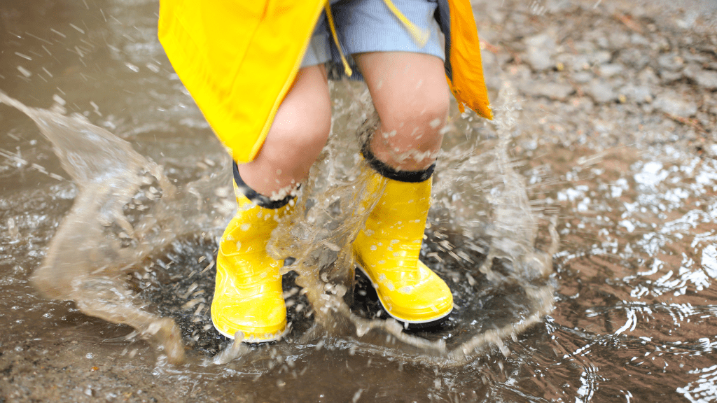 child splashing in puddles with yellow rain boots