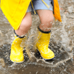 child splashing in puddles with yellow rain boots