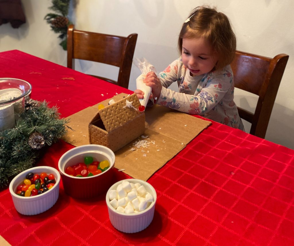 child decorating a graham cracker gingerbread house