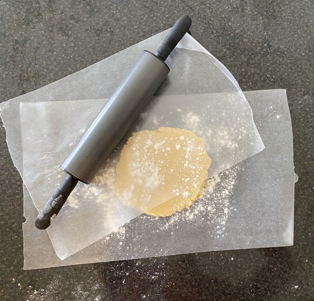 Sugar cookie dough between two sheets of wax paper with rolling pin