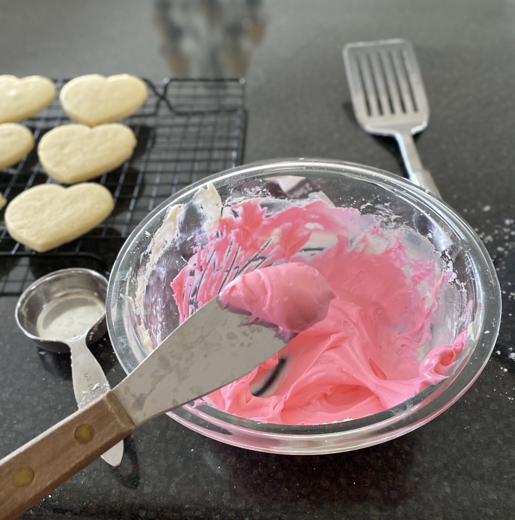 cream cheese frosting in bowl colored pink with knife 