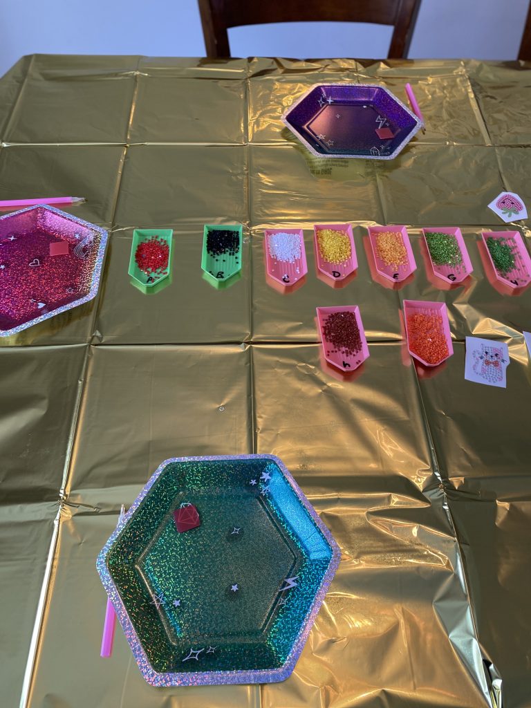 Table with gold tablecloth, jewel tone plates, and small plastic trays with gem art diamonds in them
