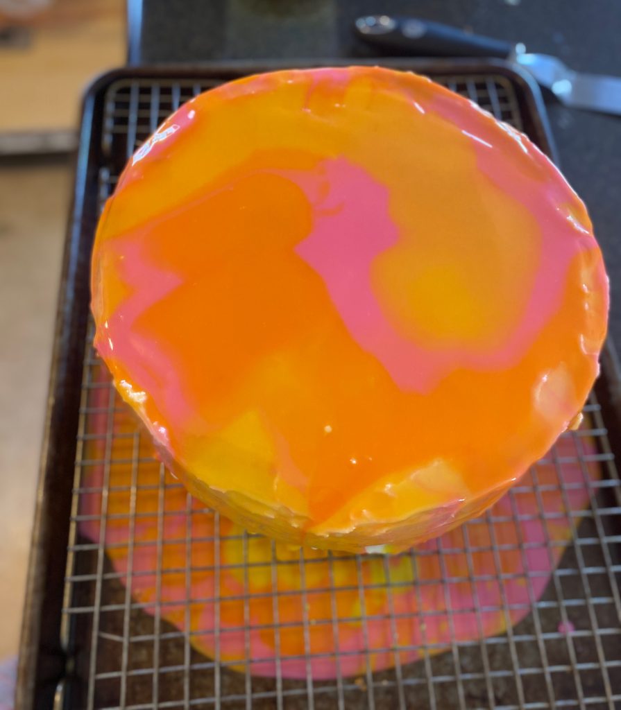 Mirror Glaze in orange, pink, and yellow poured over cake