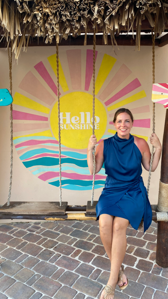 Blog Author sitting on a swing in front of a "Hello Sunshine" sign